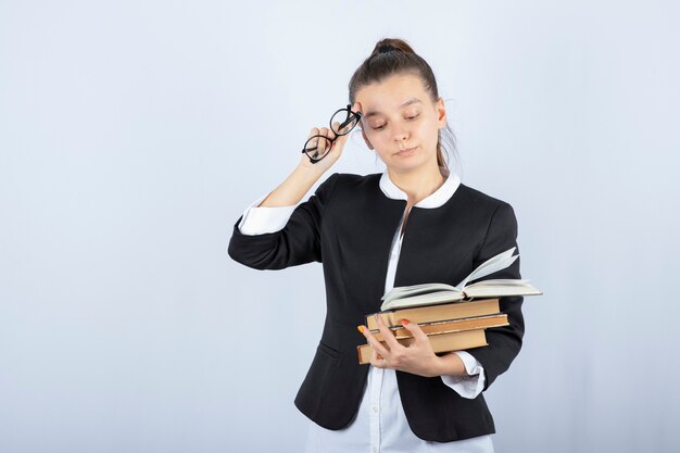 Porträt des müden Studenten, der Gläser und Bücher auf Weiß hält.