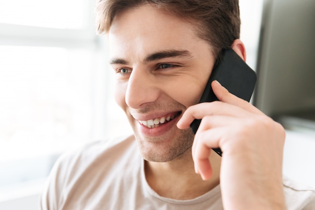 Porträt des netten attraktiven Mannes, der zu Hause am Telefon spricht