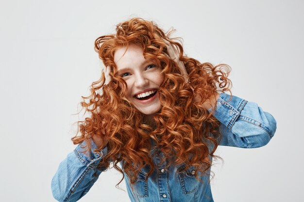 Porträt des niedlichen glücklichen Mädchens lächelnd, das ihr lockiges rotes Haar berührt.