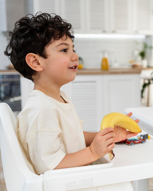 Porträt des niedlichen kleinen Jungen, der Frühstück im Kleinkindstuhl hat