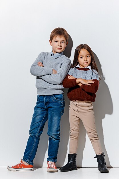 Porträt des niedlichen kleinen Jungen und des Mädchens in der stilvollen Jeanskleidung, die Kamera im Studio betrachtet