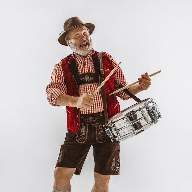 Kostenloses Foto porträt des oktoberfest-älteren mannes im hut, der die traditionelle bayerische kleidung trägt. männlicher schuss in voller länge im studio auf weißem hintergrund. die feier, feiertage, festivalkonzept. schlagzeug spielen.