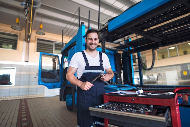 Porträt des positiv lächelnden LKW-Soldaten mit Werkzeugen, die durch LKW-Fahrzeug in der Werkstatt stehen