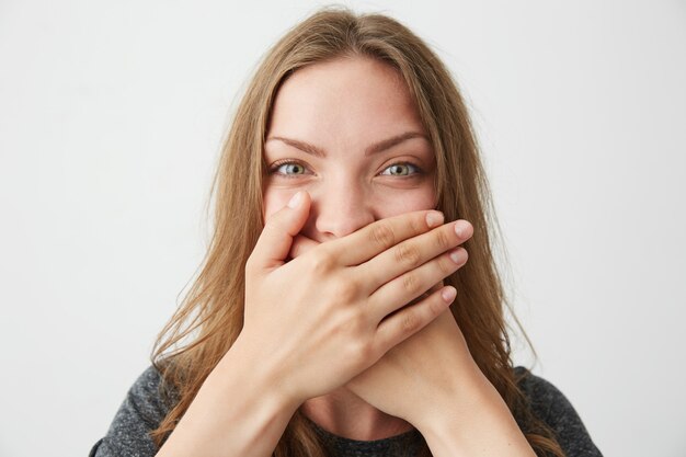 Porträt des positiven jungen schönen Mädchens, das Mund hinter Hand schließt.