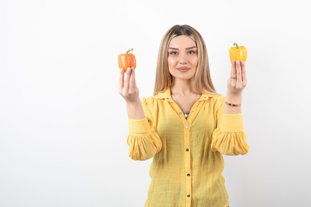 Porträt des positiven Mädchens, das bunte Paprika auf weißer Wand hält.