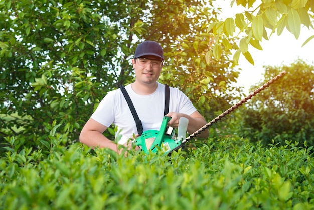 Porträt des professionellen Gärtners, der Trimmer hält, der im Hof arbeitet