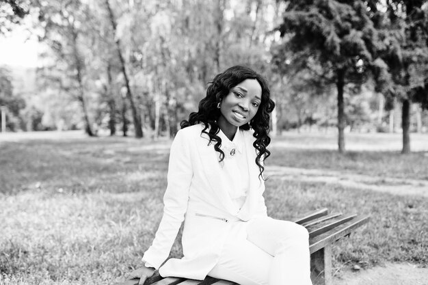 Porträt des recht schwarzen Afroamerikanermädchens, das auf Bank am grünen Park sitzt