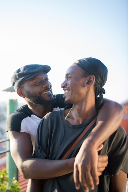 Porträt des romantischen afrikanischen schwulen Paares, das für Foto umarmt. Zwei glückliche lächelnde Männer, die auf dem Dach stehen und sich mit Vergnügen umarmen. Konzept für gleichgeschlechtliche Liebe und homosexuelle Paare