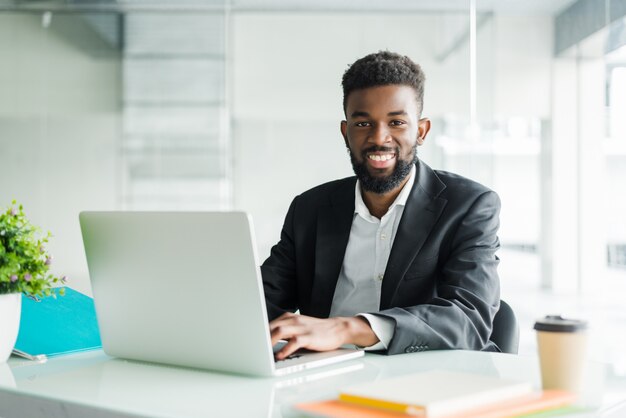 Porträt des schönen afrikanischen schwarzen jungen Geschäftsmannes, der am Laptop am Schreibtisch arbeitet