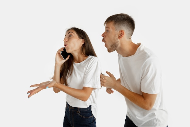 Porträt des schönen jungen Paares lokalisiert auf weißer Wand. Gesichtsausdruck, menschliche Emotionen, Werbekonzept. Frau telefoniert, Mann will ihre Aufmerksamkeit auf sich selbst richten.