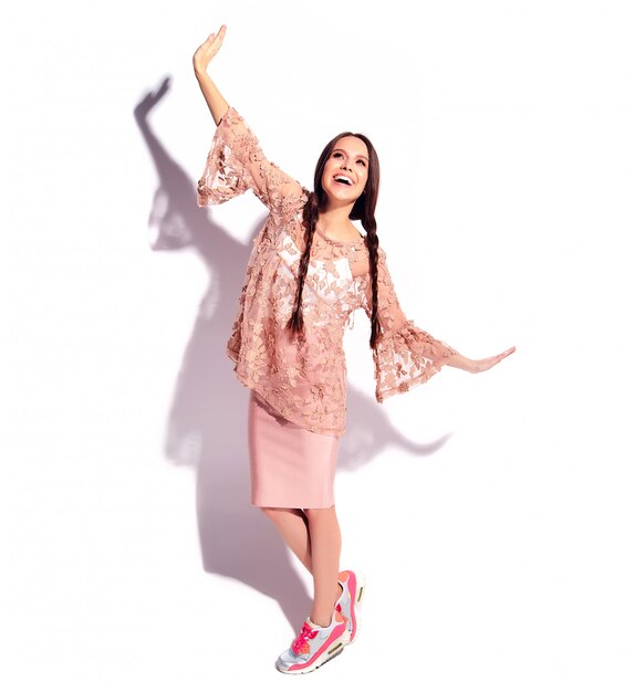 Porträt des schönen kaukasischen lächelnden Brunettefrauenmodells mit den doppelten Zöpfen in der stilvollen Kleidung des hellen rosa Sommers