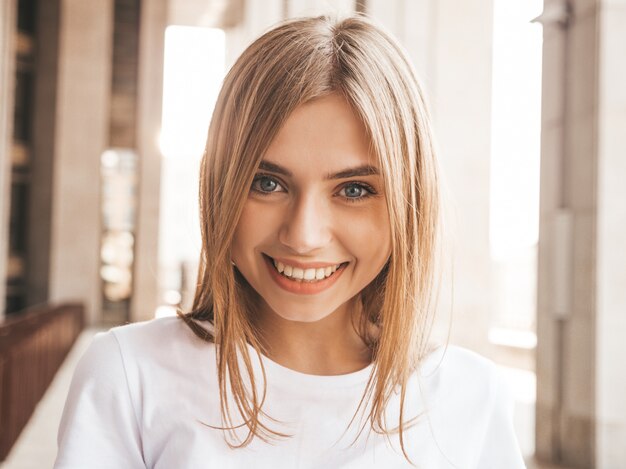 Porträt des schönen lächelnden blonden Modells kleidete in der Sommerhippie-Kleidung an. Modisches Mädchen, das im Straßenhintergrund aufwirft. Lustige und positive Frau