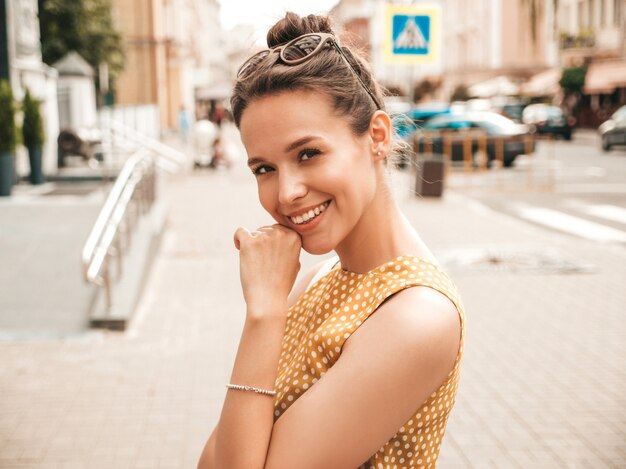 Porträt des schönen lächelnden Hippie-Modells kleidete im Sommergelbkleid an. Modisches Mädchen, das in der Straße aufwirft. Lustige und positive Frau, die Spaß hat