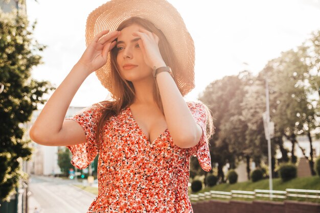 Porträt des schönen lächelnden Modells gekleidet im Sommer-Hipster-Kleid. Sexy sorgloses Mädchen, das im Straßenhintergrund bei Sonnenuntergang aufwirft. Trendige lustige und positive Frau im Hut