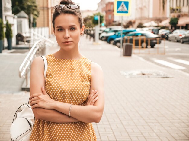 Porträt des schönen lächelnden Modells kleidete im Sommergelbkleid an. Modisches Mädchen, das in der Straße aufwirft. Lustige und positive Frau, die Spaß hat