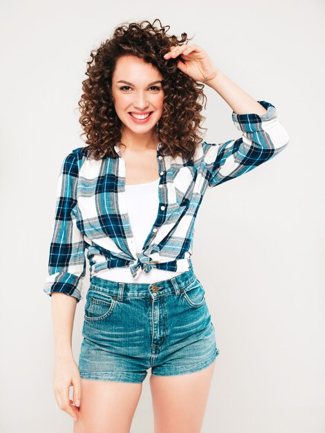 Porträt des schönen lächelnden Modells mit Afro-Lockenfrisur gekleidet in Sommer-Hipster-Kleidung. Sexy sorgloses Mädchen, das im Studio auf grauem Hintergrund aufwirft. Trendige lustige und positive Frau