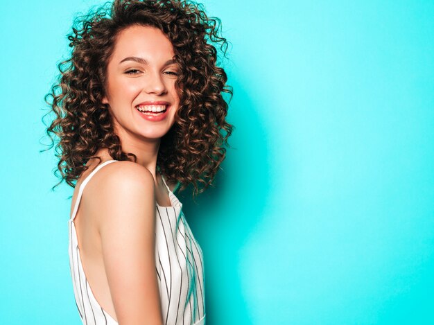 Porträt des schönen lächelnden Modells mit Afro-Lockenfrisur gekleidet in Sommer-Hipster-Kleidung. Sexy sorgloses Mädchen, das nahe blauer Wand aufwirft. Trendige lustige und positive Frau