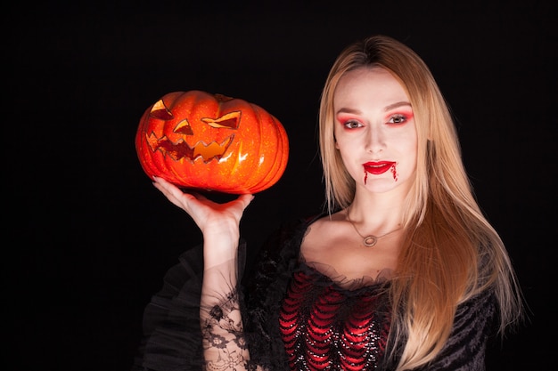 Kostenloses Foto porträt des schönen mädchens, das wie ein vampir verkleidet ist, der einen kürbis für halloween hält.