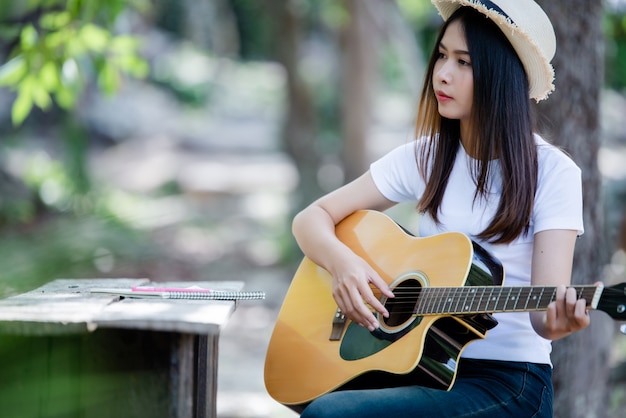 Porträt des schönen Mädchens die Gitarre mit dem Schreiben an der Natur spielend