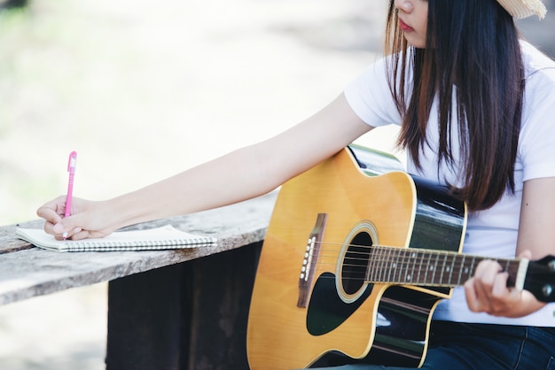 Porträt des schönen Mädchens die Gitarre mit dem Schreiben an der Natur spielend
