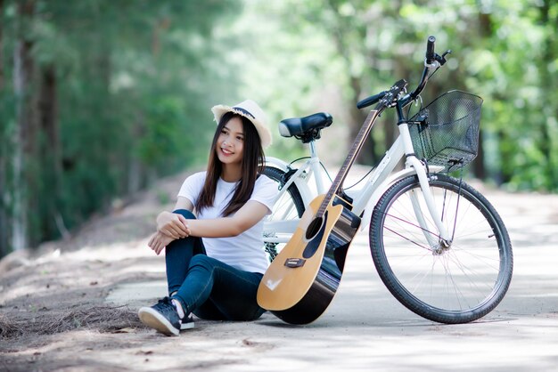 Porträt des schönen Mädchens die Gitarre mit Fahrrad an der Natur spielend