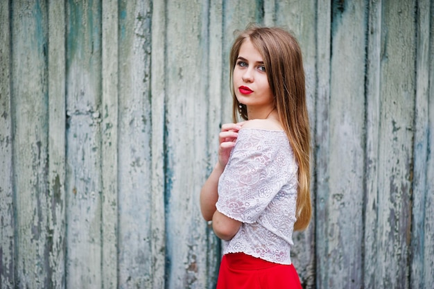 Porträt des schönen Mädchens mit den roten Lippen gegen hölzerne Hintergrundabnutzung auf rotem Kleid und weißer Bluse
