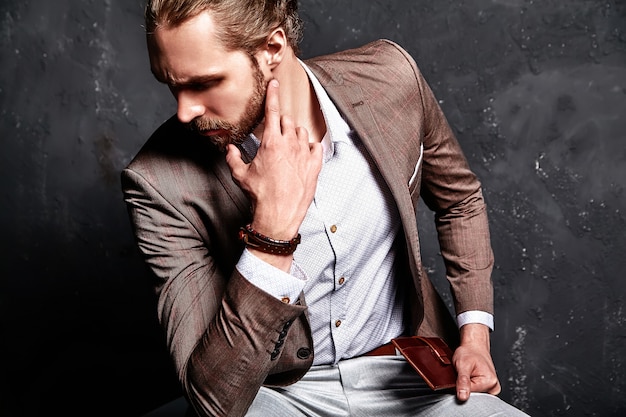 Porträt des schönen Mode stilvollen Hipster-Geschäftsmannmodells gekleidet in elegantem braunem Anzug, der nahe Dunkelheit im Studio sitzt