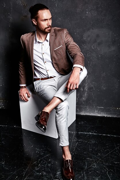 Porträt des schönen Mode stilvollen Hipster-Geschäftsmannmodells gekleidet in elegantem braunem Anzug, der nahe Dunkelheit sitzt