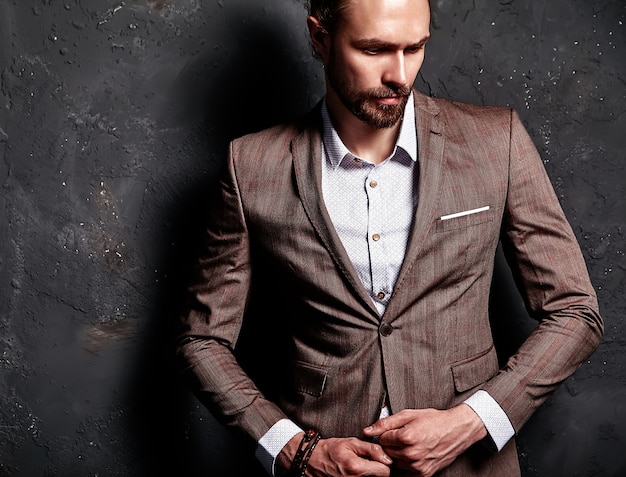 Porträt des schönen Mode stilvollen Hipster-Geschäftsmannmodells gekleidet in elegantem braunem Anzug nahe dunkler Wand