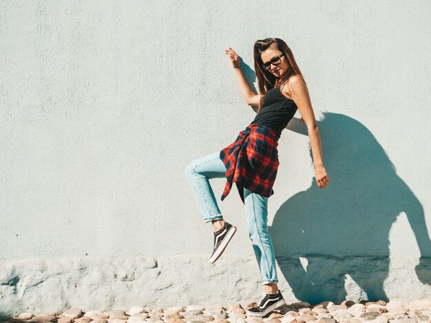 Porträt des schönen Modells. Sexy Frau gekleidet im Sommer Hipster kariertes Hemd und Jeans. Trendige Frau posiert in der Nähe der Wand auf der Straße