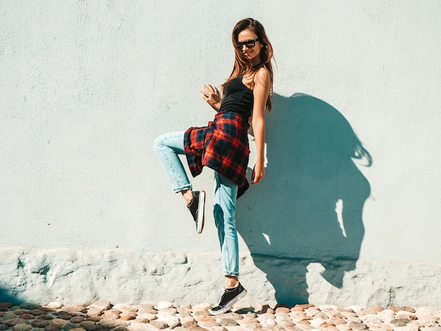 Porträt des schönen modells. sexy frau gekleidet im sommer hipster kariertes hemd und jeans. trendige frau posiert in der nähe der wand auf der straße