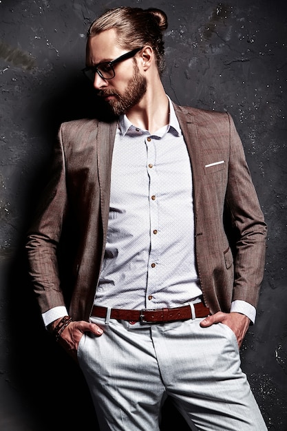 Porträt des schönen modischen Hipster-Geschäftsmannmodells der Mode, gekleidet im eleganten braunen Anzug in den Gläsern nahe dunkler Wand