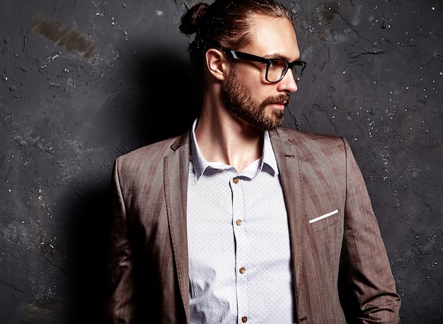 Porträt des schönen modischen Hipster-Geschäftsmannmodells der Mode, gekleidet im eleganten braunen Anzug in den Gläsern nahe dunkler Wand