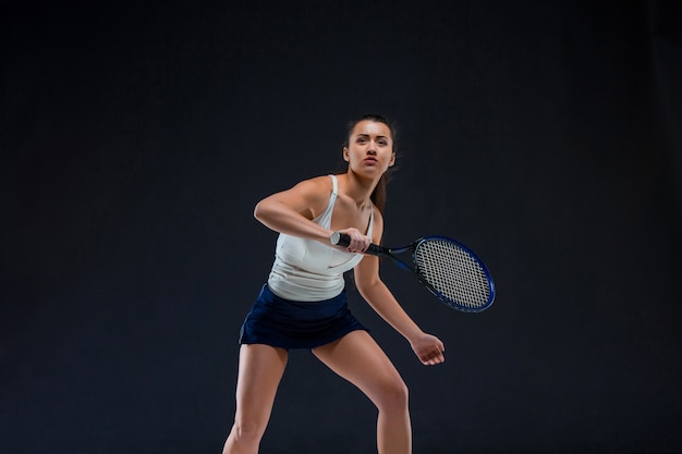 Porträt des schönen Tennisspielers mit einem Schläger an der dunklen Wand