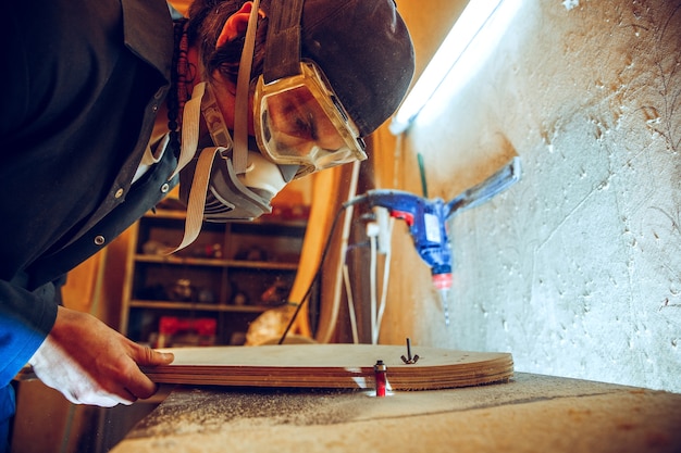 Porträt des schönen Zimmermanns, der mit hölzernem Schlittschuh an Werkstatt arbeitet, Profilansicht