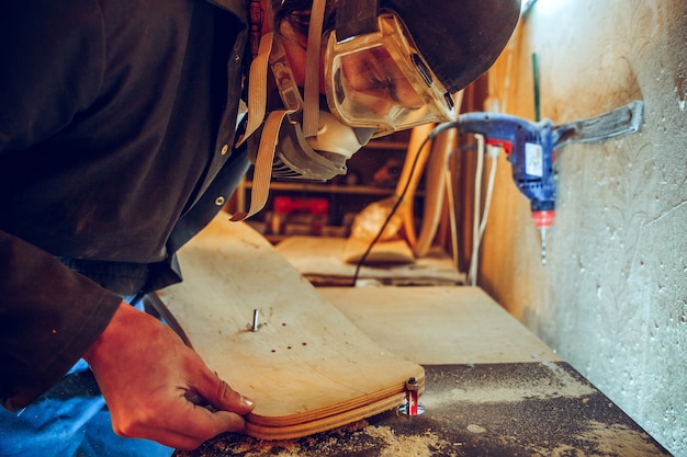 Porträt des schönen Zimmermanns, der mit hölzernem Schlittschuh an Werkstatt arbeitet, Profilansicht