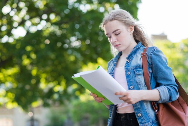 Porträt des Schulmädchens mit Buch und Tasche