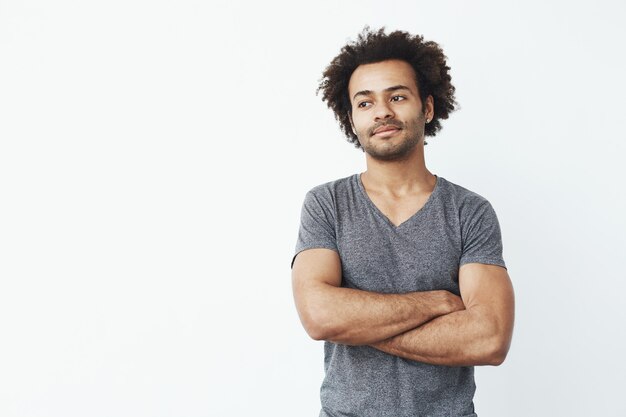 Porträt des starken und gutaussehenden afrikanischen Mannes, der links schaut und mit verschränkten Armen über weißer Wand aufwirft. Selbstbewusstes Startkonzept.