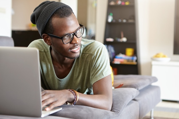 Porträt des stilvollen afroamerikanischen Mannes mit Laptop zu Hause