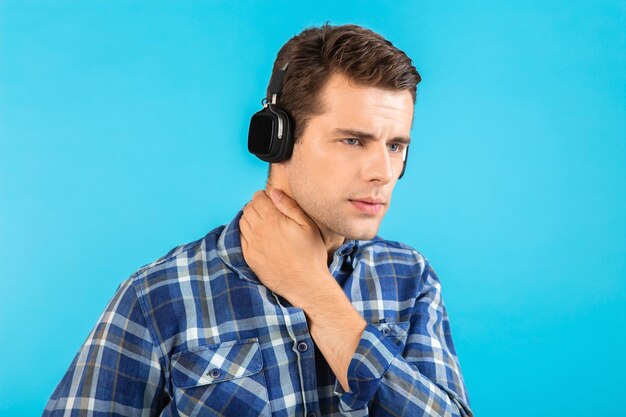 Porträt des stilvollen attraktiven gutaussehenden jungen Mannes, der Musik auf kabellosen Kopfhörern hört, die glückliche emotionale Stimmung des modernen modernen Stils glücklich auf blauem Hintergrund tragen, der kariertes Hemd trägt