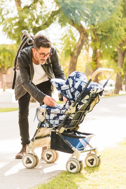 Porträt des stilvollen Mannes ihr Baby vom Spaziergänger im Park tragend