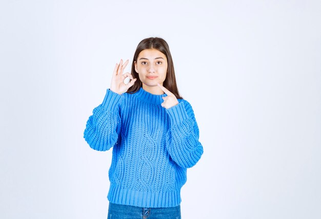 Porträt des Teenagermädchens in der blauen Strickjacke, die ok steht und gibt.