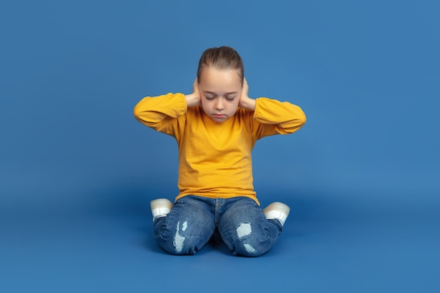 Porträt des traurigen kleinen Mädchensitzens lokalisiert auf blauem Studiohintergrund. Wie es sich anfühlt, Autist zu sein. Moderne Probleme, neue Vision von sozialen Fragen. Konzept von Autismus, Kindheit, Gesundheitswesen, Medizin.