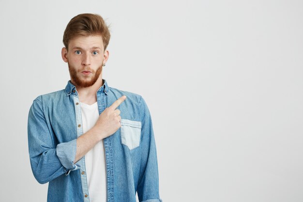 Porträt des überraschten jungen gutaussehenden Mannes, der Finger nach oben zeigt.