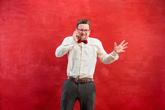 Porträt des verwirrten mannes, der per telefon einen roten hintergrund spricht