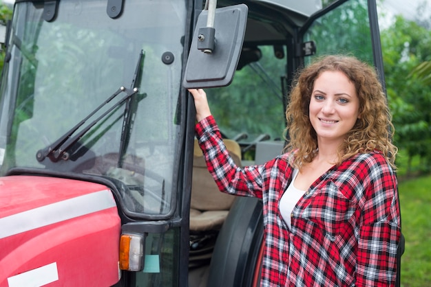 Kostenloses Foto porträt des weiblichen bauern, der durch die traktormaschine im obstgarten steht