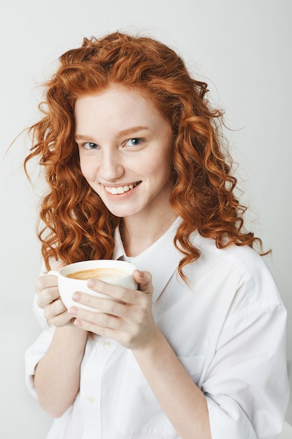 Porträt des zarten rothaarigen Mädchens mit den Sommersprossen lächelnd, die Tasse halten