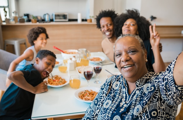 Porträt einer afroamerikanischen Familie mit mehreren Generationen, die ein Selfie zusammen nimmt, während sie zu Hause zu Abend isst.