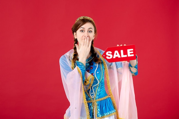 Porträt einer aserbaidschanischen Frau in traditioneller Kleidung, die das Typenschild des Verkaufs auf Rot hält