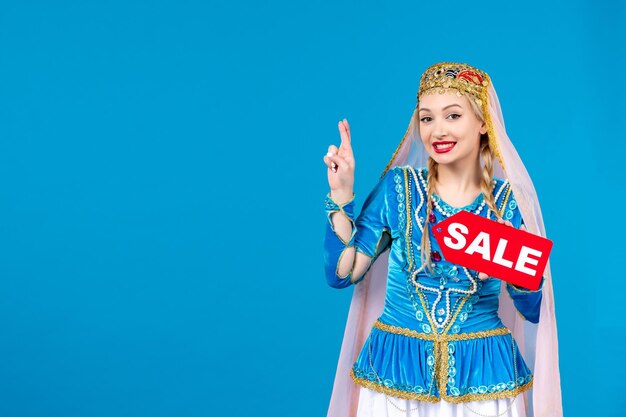 Porträt einer aserbaidschanischen Frau in traditioneller Kleidung, die ein rotes Verkaufsschild auf blauem Hintergrund hält, ethnisches Einkaufen novruz